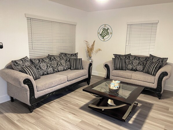 Ein Wohnzimmer mit zwei grauen Sofas, Kissen in Schwarz-Weiß-Muster, einem Glastisch und einer Wanddekoration mit einer Schildkröte.