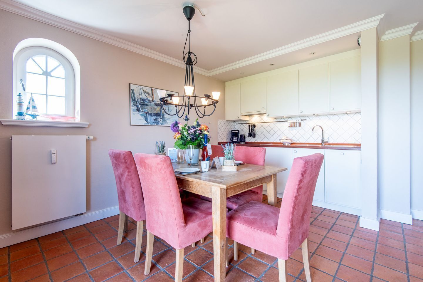 A dining area with a wooden table and pink upholstered chairs, a chandelier, and a window with a view.