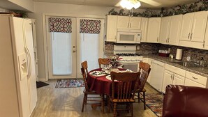 A compact kitchen with white cabinets, a microwave, and a stove. There is a dining table with chairs and a red tablecloth.
