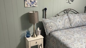 A bedroom with a bed, a nightstand with a lamp, a tissue box, and a wall art piece.