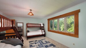 Une chambre avec des lits superposés, une fenêtre donnant sur les arbres, un escalier en bois et un tapis à motifs.