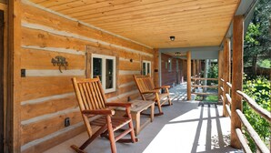 Une cabane en bois dotée d’un porche avec des fauteuils à bascule et d’une clôture en bois.
