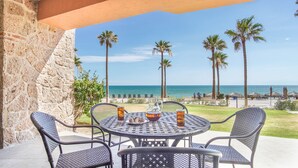 Une terrasse avec une table et des chaises donnant sur une plage bordée de palmiers et sur l’océan.