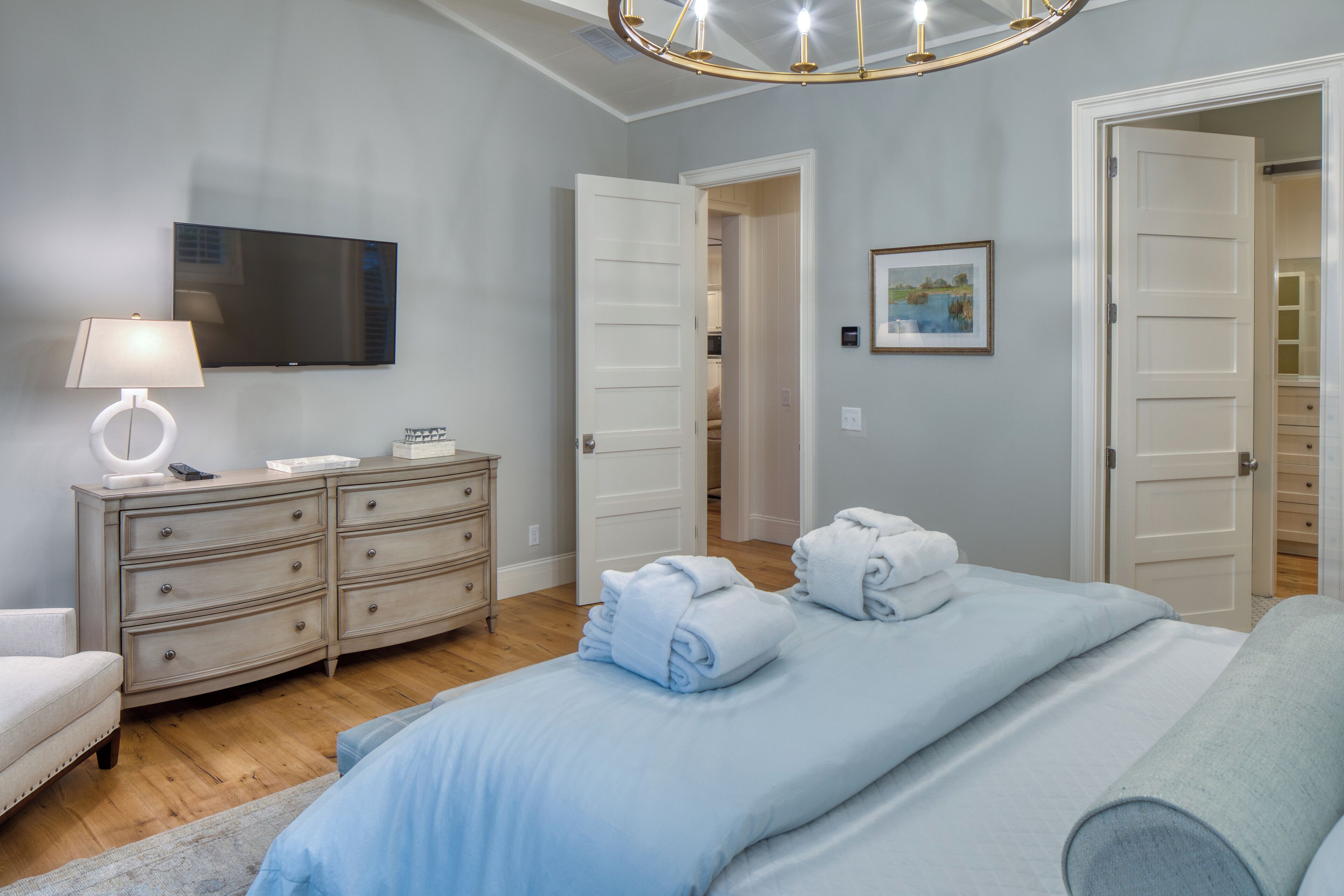 Un dormitorio con cama, cómoda, lámpara, televisor y puerta que da a otra habitación.