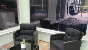 A covered patio area with wicker furniture, a glass table, and a view of a pool and outdoor seating. - Emerald House : Free Amazing Heated Pool !!!!! (Bradenton)