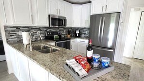 A modern kitchen with white cabinetry, a granite countertop, stainless steel appliances, and a built-in island with a sink and storage. - Emerald House : Free Amazing Heated Pool !!!!! (Bradenton)