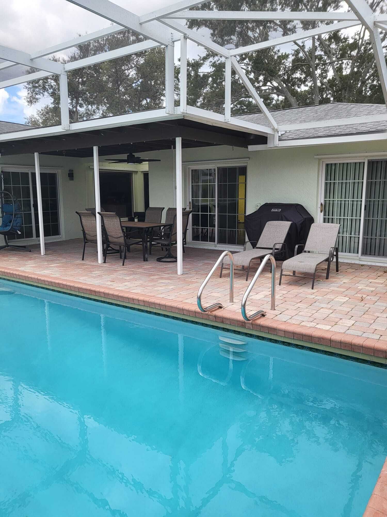 Un espace aménagé au bord de la piscine, avec un patio couvert, des sièges d’extérieur et un barbecue.