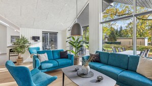 Ein geräumiges Wohnzimmer mit großem Fenster, einem blauen Sofagarnitur, einem Couchtisch und einem Blumentopf.