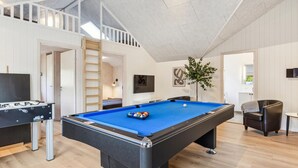 Ein Billardtisch in einem Raum mit Holzboden, einer Couch, einem Fernseher und einer Treppe.