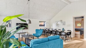 Ein großzügiger Wohnbereich mit hohen Decken, einem Esstisch mit Stühlen, einem blauen Sofa und einer großen Küsterpflanze.
