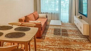 A modern living room with a sofa, a coffee table, a TV, and a dining area with placemats.
