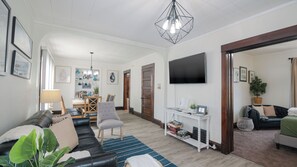 A spacious living room with a sofa, armchairs, a coffee table, and a TV mounted on the wall. There is a dining area in the background with a table and chairs. - 3 Blocks from Beach house 1 BDRM full bath 4 min to downtown,sleeps 4 (Sheboygan)