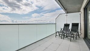 A balcony with two chairs, a glass railing, and a view of the sky. - Haus Sommertraum, Appartement 5 "sonnensegel" - Haus Sommertraum (Scharbeutz)