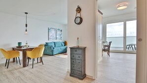 A modern living room with a sofa, a dining table with chairs, and a large window. - Haus Sommertraum, Appartement 5 "sonnensegel" - Haus Sommertraum (Scharbeutz)