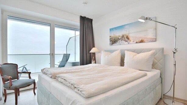 A hotel room with a large bed, a chair, a desk, and a view of the sea through large windows. - Haus Sommertraum, Appartement 5 "sonnensegel" - Haus Sommertraum (Scharbeutz)