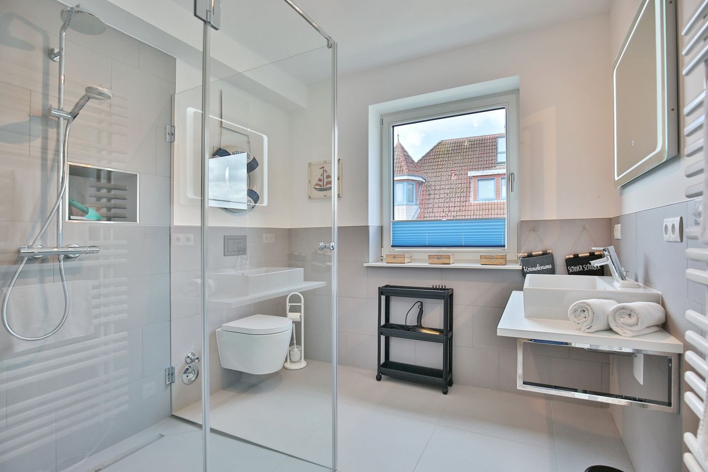 A modern bathroom with a glass shower enclosure, a toilet, a sink, and a window with a view of buildings.