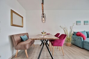 Un soggiorno moderno con un tavolo da pranzo in legno, due poltrone in velluto, un divano in pelle marrone e un divano verde acqua con cuscini rossi.