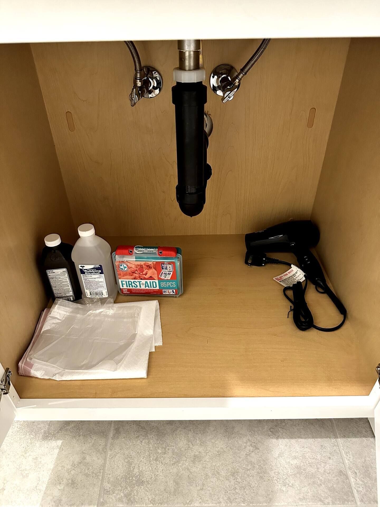 Un área de lavamanos con grifo, una caja de botiquín de primeros auxilios, dos botellas de alcohol isopropílico, un secador de pelo y una bolsa de plástico.