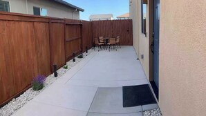 Un patio con cerco de madera, mobiliario exterior y una puerta que da a un edificio.