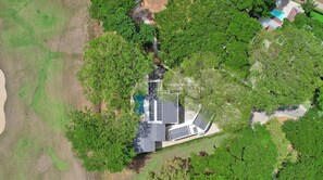 Vista aérea de una casa moderna con techo de paneles solares, rodeada de vegetación densa y una piscina.