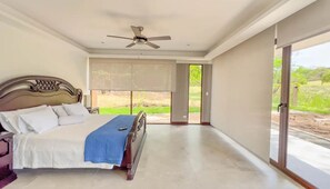 Un dormitorio con cama, ventilador de techo, ventana grande y vistas al exterior.