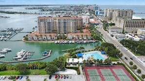 Un paisaje urbano costero con un puerto deportivo, hoteles de gran altura y una cancha de tenis.