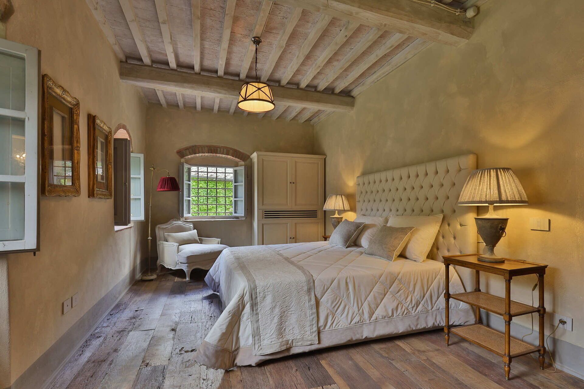 Une chambre à coucher avec un grand lit, une table de chevet, une armoire et une fenêtre donnant sur un paysage verdoyant.