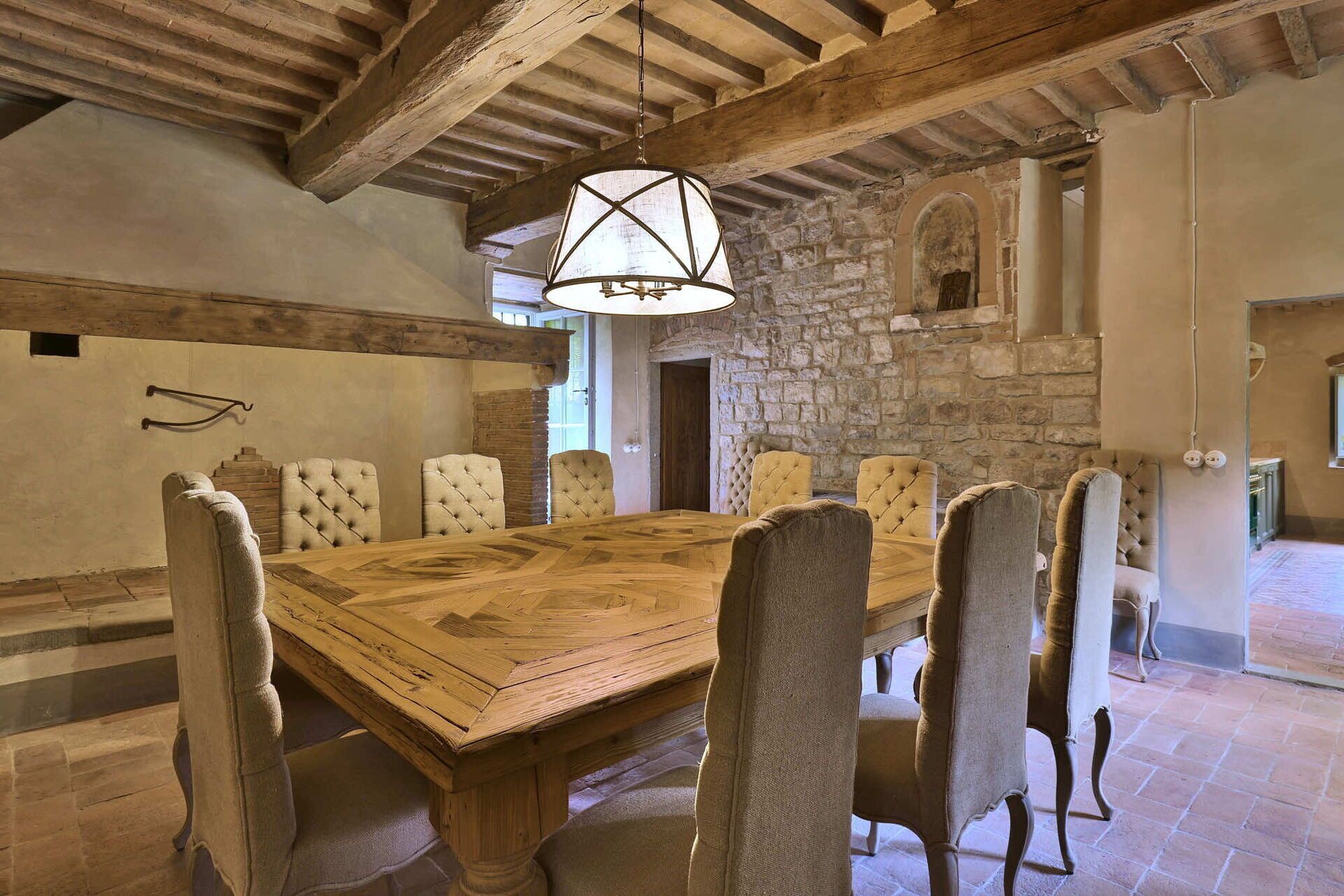 Un comedor rústico con una gran mesa de madera rodeada de sillas tapizadas, paredes de piedra y vigas de madera a la vista.