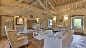 Een ruime woonkamer met een hoog houten plafond, een open haard en een groot raam dat zorgt voor veel daglicht.
