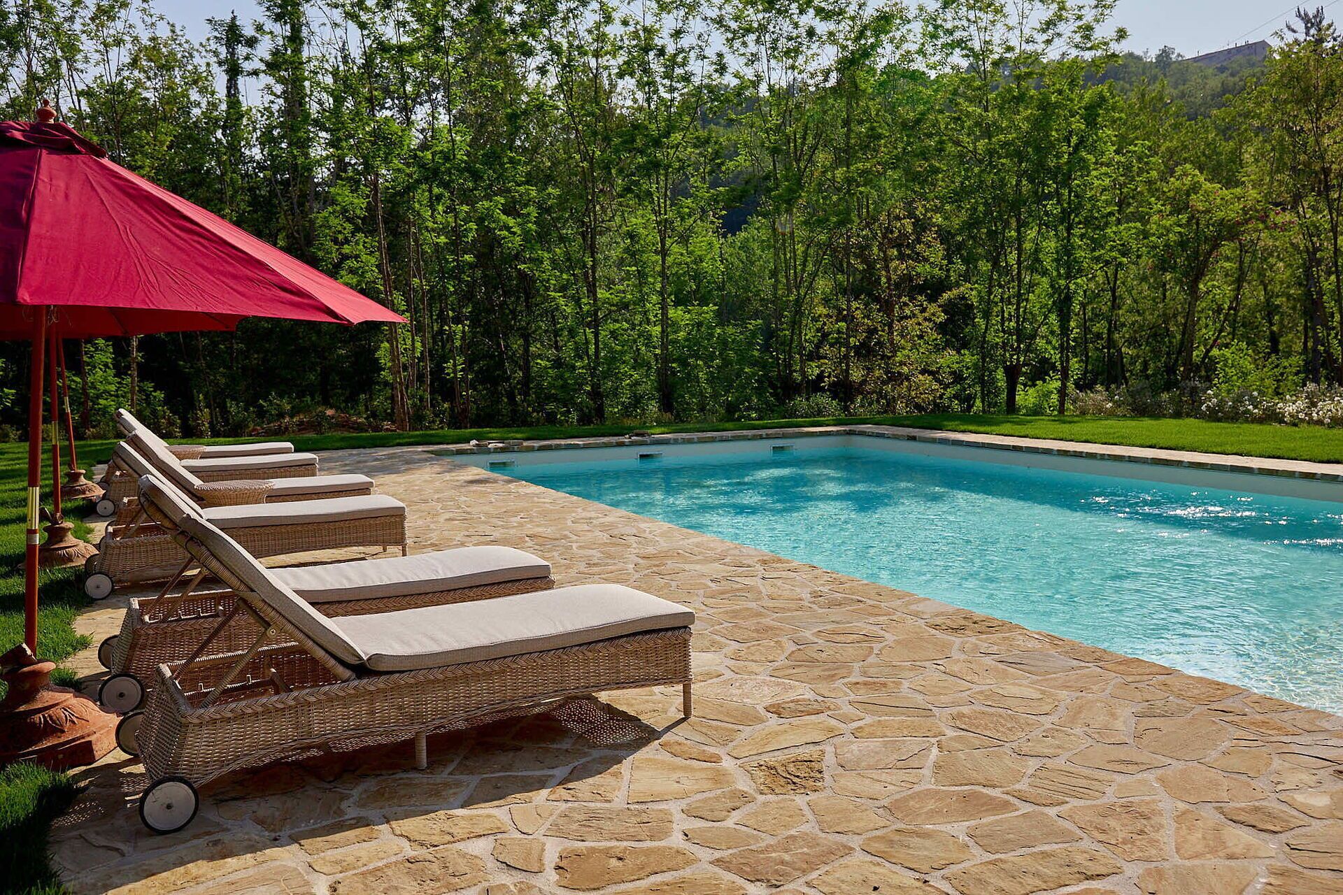 A swimming pool with lounge chairs and a red umbrella.