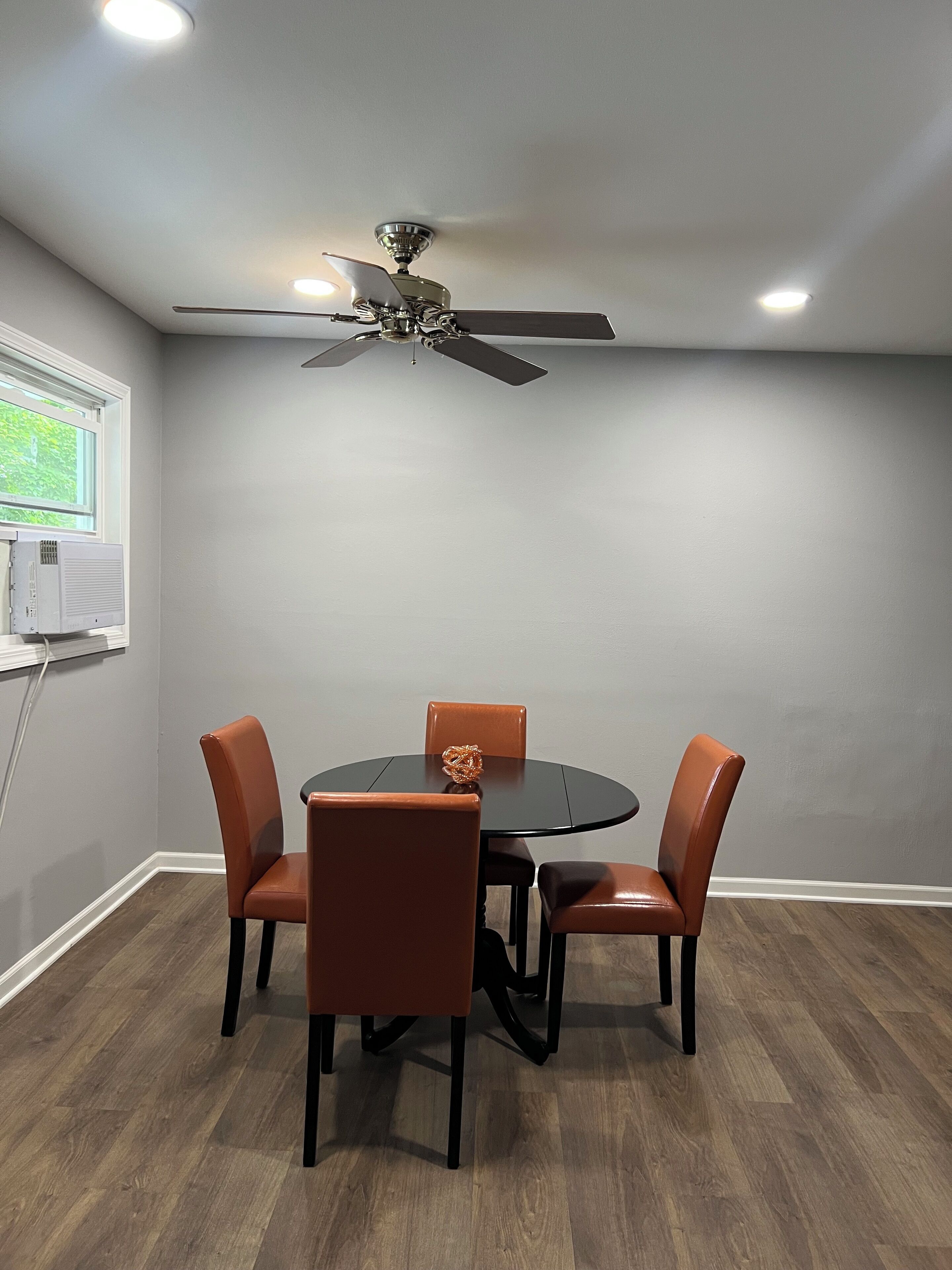 A conference room with a round table, four chairs, a ceiling fan, and a window with blinds.