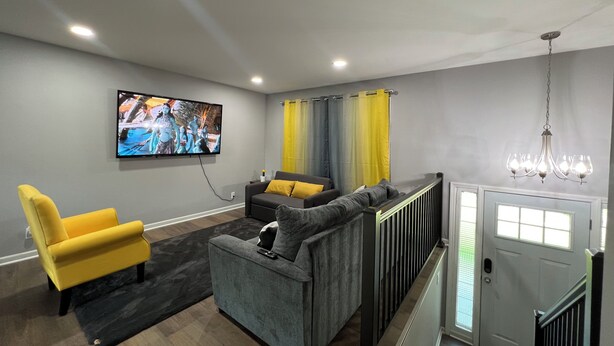 Una sala de estar moderna con un sofá gris, un sillón amarillo y un televisor de pantalla plana montado en la pared.