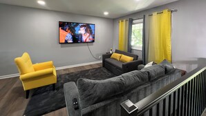 Una sala de estar moderna con un sofá gris, un sillón amarillo y un televisor de pantalla plana montado en la pared.