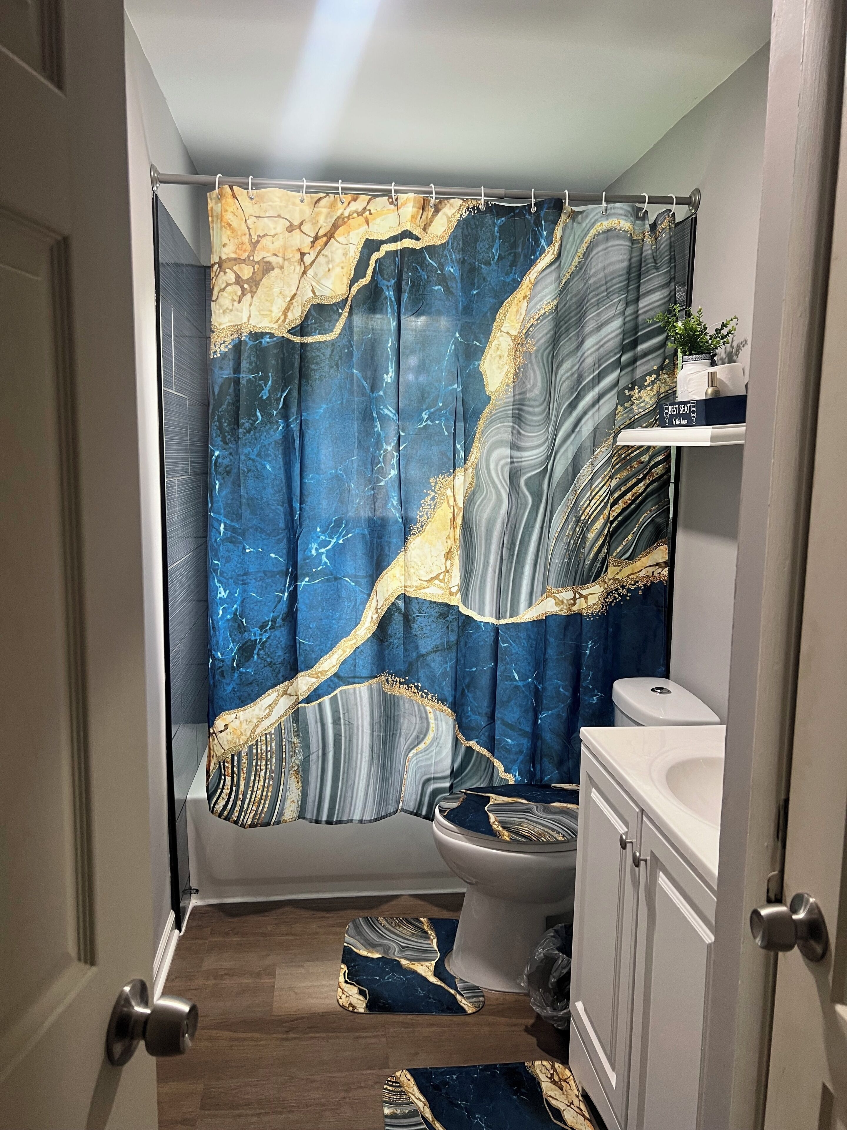 Un bagno con tenda da doccia a effetto marmo, un water, un lavandino e un piccolo ripiano con articoli da toilette.