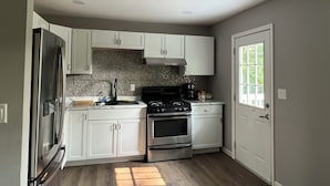 Una cocina compacta con armarios blancos, un refrigerador de acero inoxidable, una estufa negra y un salpicadero de azulejos.