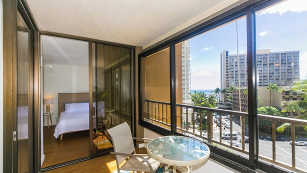 Quarto de hotel com varanda, cama, cadeira e mesa.