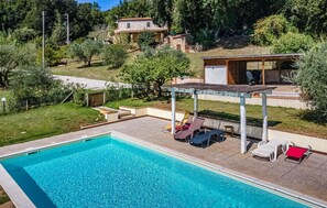 Une piscine dotée de chaises longues et d’une pergola, entourée d’une pelouse et d’arbres.