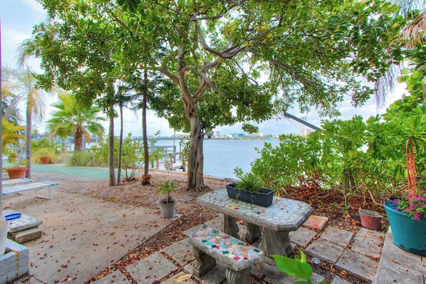 A patio area with a stone table, potted plants, and a view of the water.