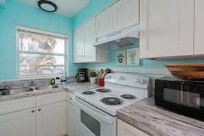 A kitchen with white cabinets, a white stove, a black microwave, and a window with a view of palm trees.