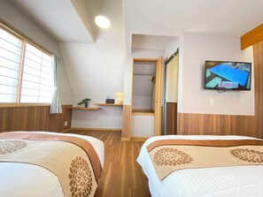 A hotel room with two beds, a TV on the wall, a window with blinds, a shelf with a plant, and a wooden door leading to a bathroom. - N9#Good Location + Clean Room! in Shinjuku (新宿区)