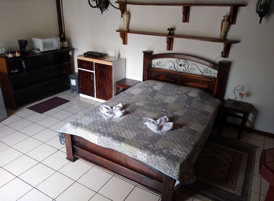 Un dormitorio con cama de madera, una mesita de noche pequeña, un escritorio con silla y un microondas sobre un mueble.