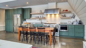 A modern kitchen with green cabinets, a central island with chairs, and built-in appliances. - Saddleback - Parmachenee A-Frame #1 - SkiFrame (Sandy River Plantation)