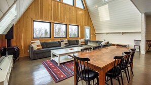 A spacious loft with a high ceiling, wooden walls, a large dining table, and a cozy seating area with a sofa and chairs. - Saddleback - Parmachenee A-Frame #1 - SkiFrame (Sandy River Plantation)