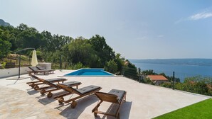Un espace aménagé au bord de la piscine, avec des chaises longues et une piscine donnant sur une étendue d’eau.
