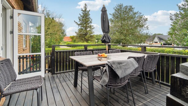 An outdoor patio with a table and chairs, a covered umbrella, and a view of the surrounding greenery and buildings. - Lovely home in Samsø with WiFi (Samsø)