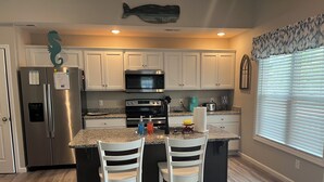A modern kitchen with white cabinets, stainless steel appliances, and a granite countertop. - Only TWO MILES to the beach! Custom bungalow. Fenced-in yard! (Ocean Isle Beach)