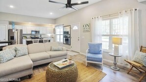 A modern living room with a sofa, armchairs, a coffee table, and a dining area with a kitchen in the background. - Only TWO MILES to the beach! Custom bungalow. Fenced-in yard! (Ocean Isle Beach)