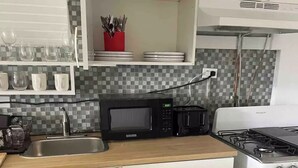 Una cocina compacta con microondas, estufa y distintos utensilios de cocina.