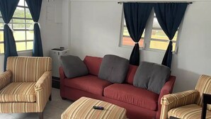 Una sala de estar con sillones a rayas, un sofá rojo y un reposapiés a juego.