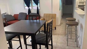 Un espacio habitable compacto con comedor, un sofá, un sillón a rayas y una zona de cocina con taburetes.